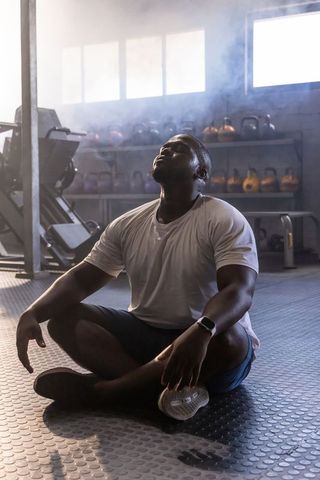 African american man resting after strength training in industrial gym, backlit dramatic light