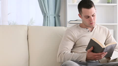 Man Relaxing on Sofa Reading Thoughtfully