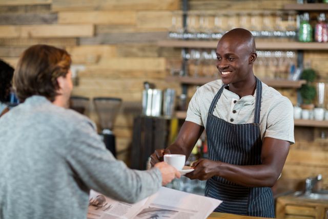Smiling waiter serving cup of coffee to man at counter in cafÃ©