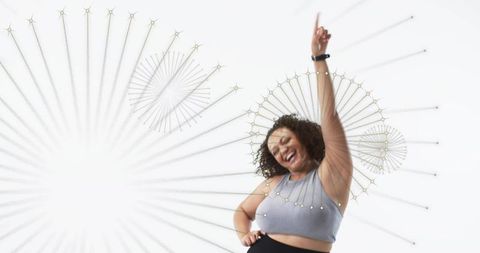 Joyful plus size woman dancing with smartwatch on minimalist radial geometric background