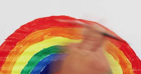 Hand painting vibrant rainbow on white canvas
