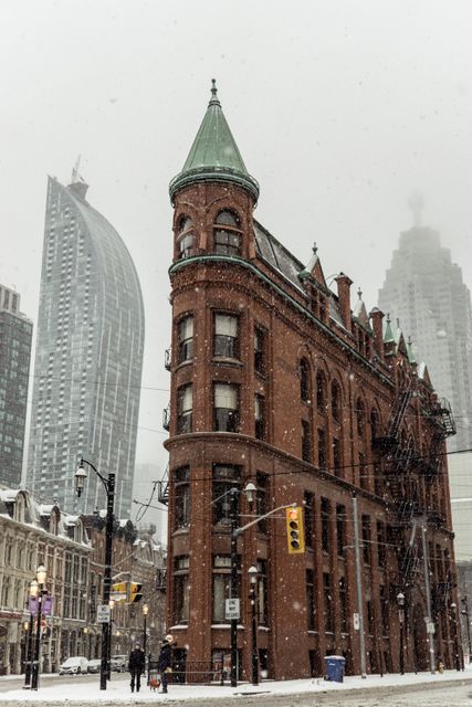 Historic building stands prominent amid light snowfall with modern skyscrapers rising in background. Snow falling lightly creates a serene scene blending past and present urban architecture. Suitable for urban winter scenes, contrasts between old and modern architecture, or promoting city tourism in winter.