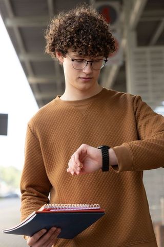 Teen commuter checking watch while holding spiral notebook on transit platform