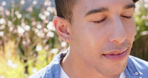 African man meditating in sunny meadow closing eyes wearing hoop earrings soft bokeh