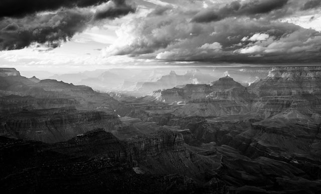 Dramatic black and white landscape of the Grand Canyon with stormy clouds overhead. Perfect for use in travel promotions, nature documentaries, art collection, wall art, nature magazine features, and presentations showcasing dramatic natural landscapes.