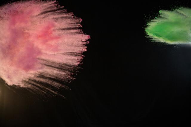 This image depicts a dynamic and colorful burst of pink and green powder against a black background. Ideal for use in advertisements, festival promotions, creative projects, and design backgrounds where a vibrant, energetic visual is required.
