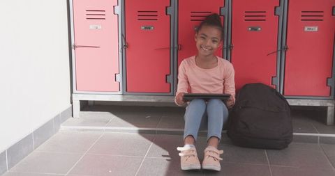 Girl Using Tablet Near Red Lockers in School Corridor