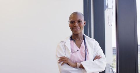Confident female physician standing with arms crossed in modern clinic wearing white coat