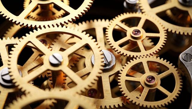 Meshing brass gears turning with polished screws and ruby jewels in macro clockwork detail