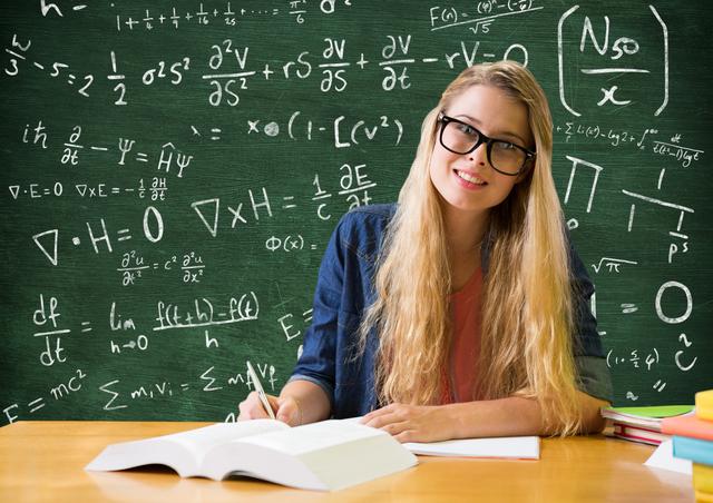 Young woman sitting at desk in classroom, writing in notebook with mathematical equations on blackboard behind her. Ideal for educational content, tutoring services, academic websites, and promotional materials for schools or learning centers.