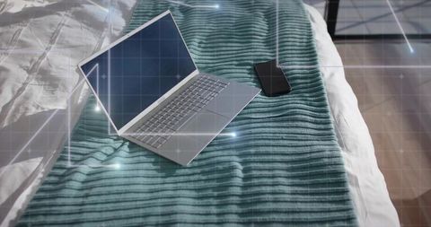 Silver laptop and smartphone resting on teal blanket displaying augmented reality grid