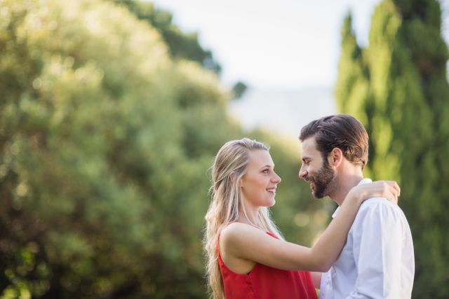 Blonde woman and bearded man sharing a joyful moment in a green park. Perfect for themes related to romance, love, and happiness. Useful for advertisements, relationship blogs, greeting cards, or social media promotions.