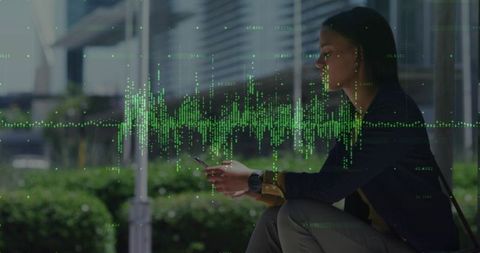 Businesswoman sitting on urban bench holding smartphone with green data overlay and glass panels