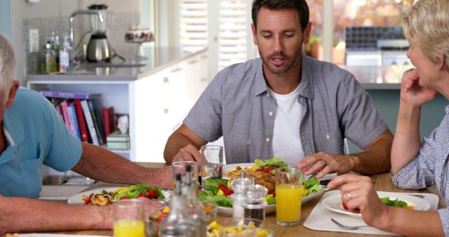 Family members sitting around kitchen table, engaging in a casual breakfast meal. Various food items and glasses of juice are on the table. Suitable for use in articles or advertisements about family life, morning routines, healthy breakfasts, and domestic settings.