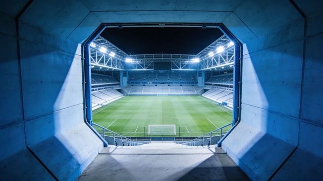 Framing octagonal tunnel revealing illuminated football stadium at night with centered goal