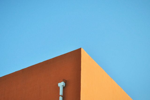 Featuring corner of a modern building with stark geometric lines against bright blue sky. Bold colors and minimalistic composition create visually striking and dynamic image. Perfect for use in architectural portfolios, urban design presentations, marketing materials, and creative projects requiring vibrant visuals.
