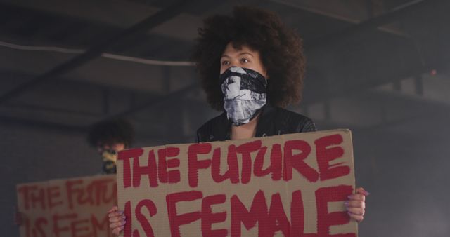 Woman with curly hair holding a sign reading 'The Future is Female'. Wearing bandana on face, expressing strong and fearless stance. Suitable for projects on gender equality, feminism, women empowerment, social activism, and human rights causes.
