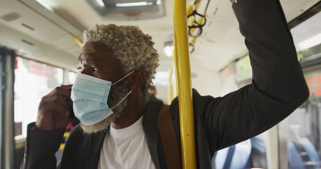 African american senior man wearing face mask talking on smartphone while standing in the bus. hygiene and social distancing during coronavirus covid-19 pandemic.