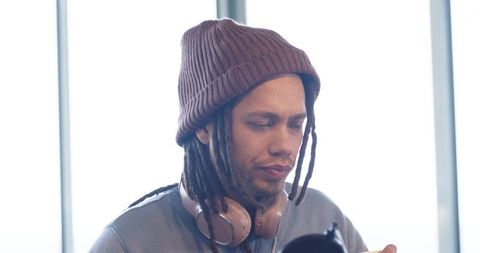 Mid-adult african american musician adjusting microphone by window with beanie and headphones