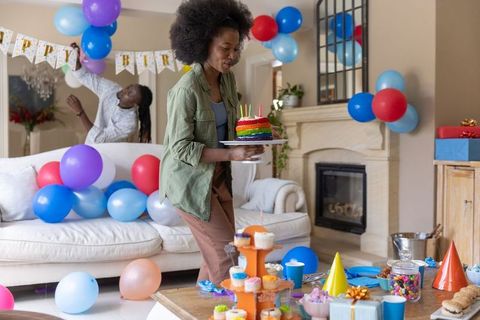 African american family preparing colorful birthday party with rainbow cake and balloons
