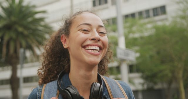 Portrait of happy biracial woman in city, wearing headphones and smiling. digital nomad on the go, out and about in the city.