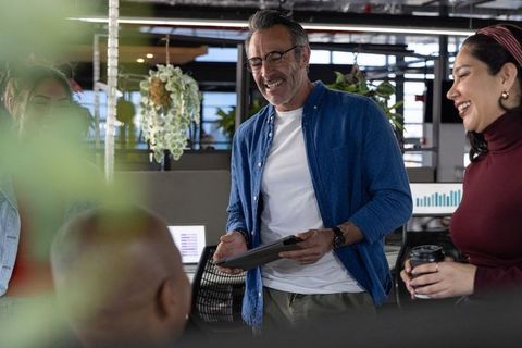 Multicultural team collaborating and smiling around desk with tablet in modern open office