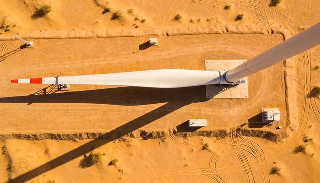 Top-down view of single wind turbine blade stretching across golden desert with red tip