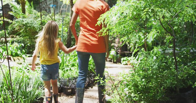 Caucasian mother and daughter holding hands and walking in sunny garden. Family, nature, gardening and hobbies.
