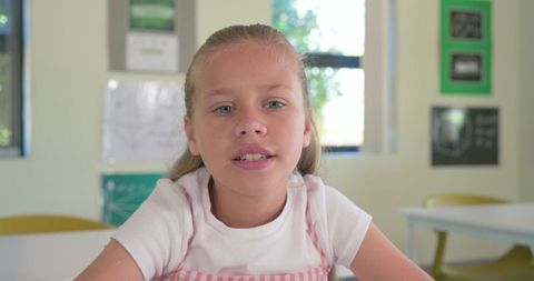 Preteen girl speaking at classroom desk wearing pink gingham pinafore