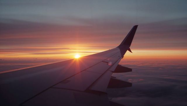 Airplane Wing Glowing in Sunrise Over Clouds