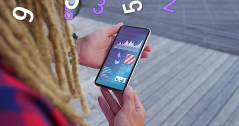 Man with dreads holding smartphone showing mobile analytics dashboard on wooden boardwalk