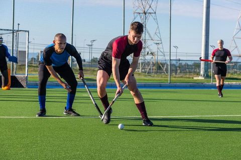 Competitive male athletes playing field hockey on turf