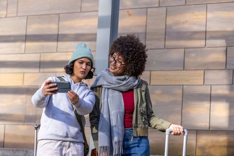 Multicultural friends taking selfie with luggage at sunny urban train station