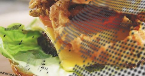 Melting cheddar dripping over juicy burger with crispy onion rings on halftone wrapper
