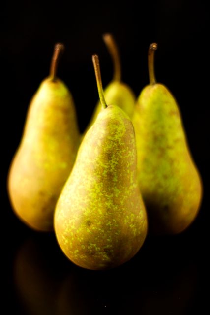 Photo shows four ripe green pears against a dark background, with a focus on their natural speckled texture. Great for use in food blogs, market advertisements, or health and nutrition articles to promote organic produce and healthy eating. Ideal for illustrating autumn harvests or depicting still life compositions.