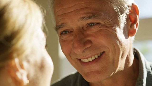Warm senior man smiling at partner by window close-up natural light portrait of affection