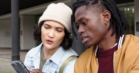 Multiracial friends checking smartphone together while discussing plans and directions