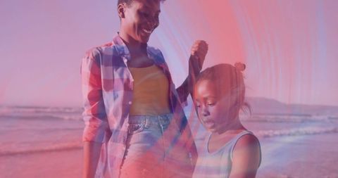 Mother and daughter sharing tender beach moment adjusting hair in warm sunset light