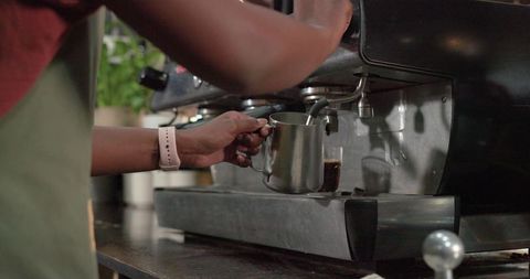 Barista steaming milk with pitcher under steam wand on espresso machine at counter