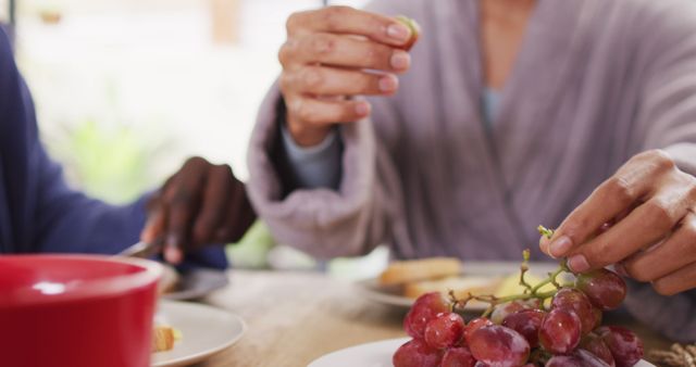 Two people, possibly a couple, sharing a fresh and healthy breakfast of grapes and toast. Image focuses on their hands, highlighting the act of picking grapes and spreading toast. Perfect for use in health and nutrition blogs, relationship and lifestyle articles, and advertisements promoting relaxing morning routines.