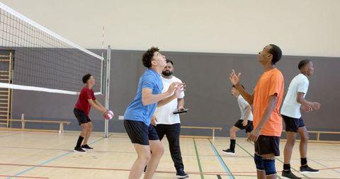 Diverse male volleyball team practicing indoors with coach holding clipboard