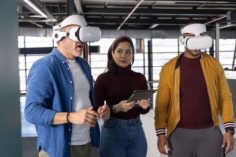 Diverse team testing virtual reality headsets in modern office with woman holding tablet