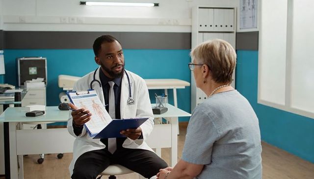 Physician consulting senior patient in clinic holding clipboard explaining medical chart