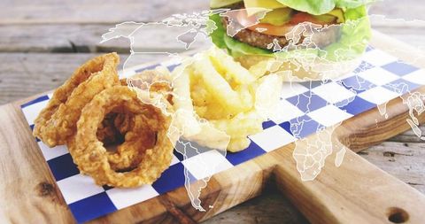 Serving crispy onion rings and curly fries plus burger on rustic board featuring world map overlay