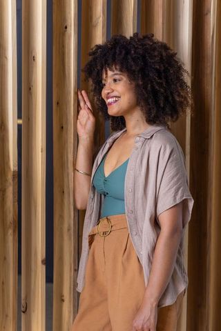 Smiling african american woman standing by wooden slats wearing teal top and linen shirt
