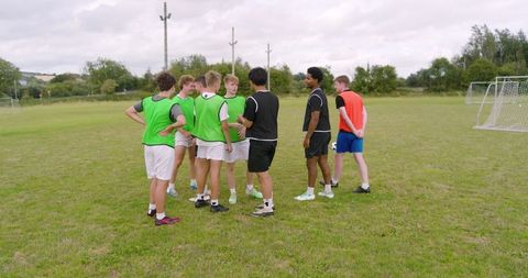 Teen soccer team strategizing on field with training bibs