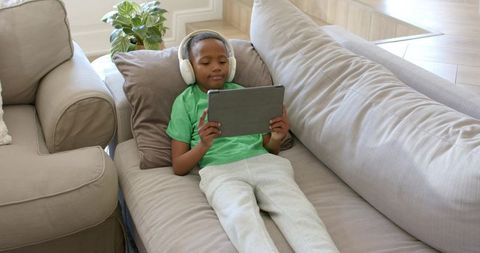 Boy Relaxing on Couch Using Tablet and Headphones at Home for Learning and Entertainment