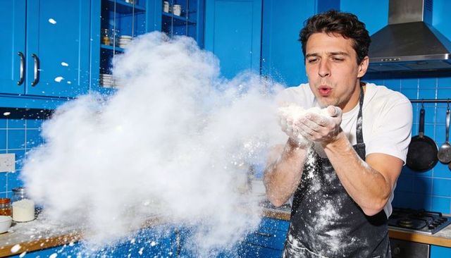 Home baker blowing flour cloud in bright blue kitchen playful baking moment