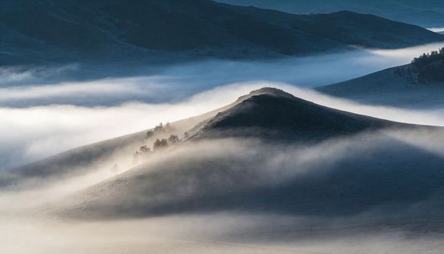 Conical Hill Emerging from Morning Mist Over Layered Ridges at Dawn