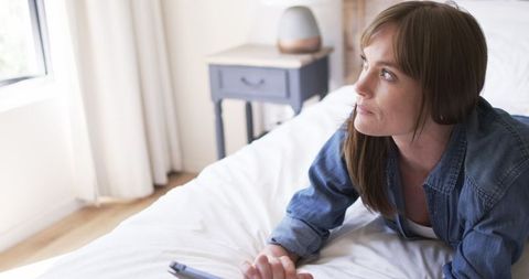 Thoughtful Middle-aged Woman Daydreaming in Sunny Bedroom